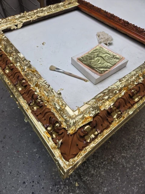 Blattgold wird mit dem Anschießer auf das Poliment gelegt, daneben Goldheft und Wattebausch
