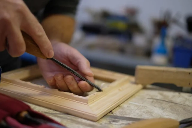 Hand führt das Schnitzeisen an einer Rahmenleiste im Atelier